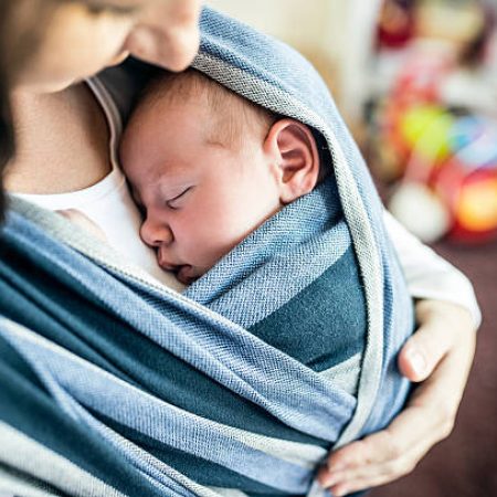 Close up of unrecognizable young mother with her newborn baby son in sling at home